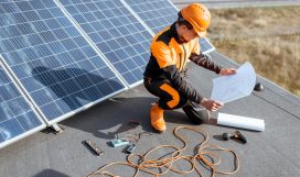 Electrician installing solar panels Electrician in protective workwear installing solar panels, sitting on a rooftop with blueprints and working tools